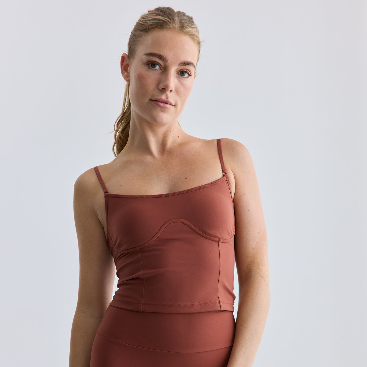 Woman wearing a brown tank top against a light gray background