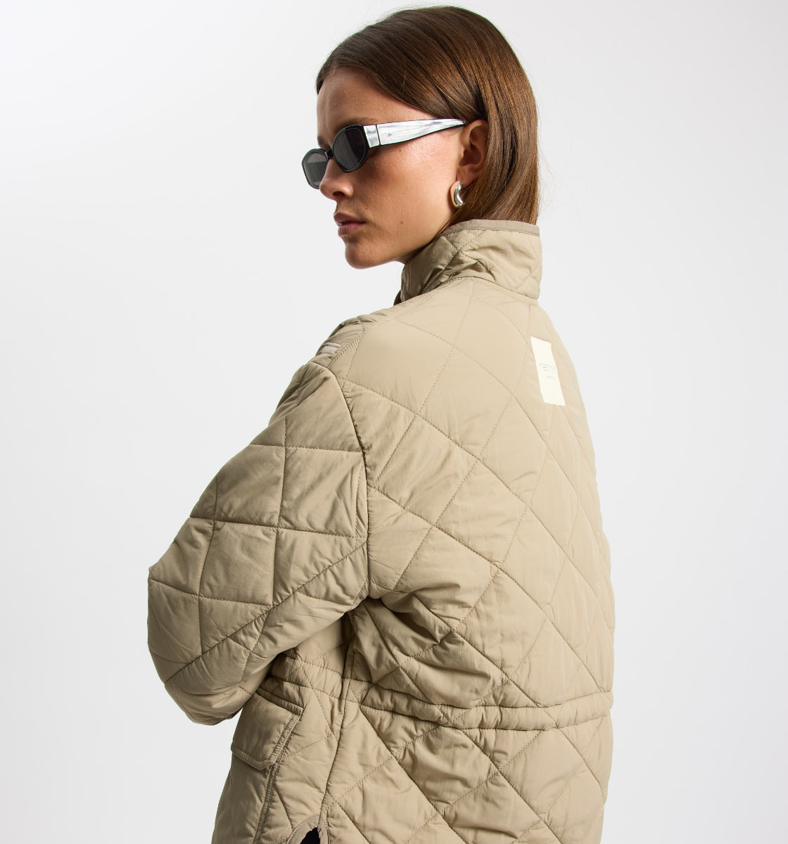 Person wearing a beige quilted jacket on a white background